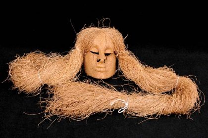 Máscara Buriti feita de fibras, recebida pelo Museu em 1989. Sobre a cabeça do ornamento prende-se muitos fios de buriti que caem longos e compridos, representando cabelos. Possui um laço de fita na cor vermelha de cada lado que prende os fios.